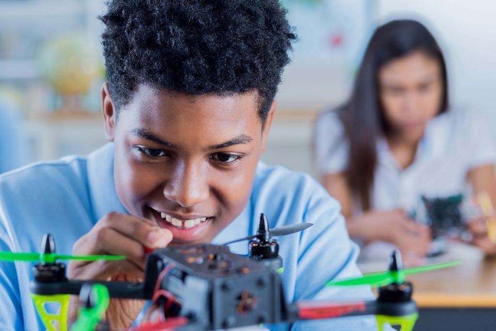 Two students in a classroom working on assembling drones, with one showing green propellers prominently.