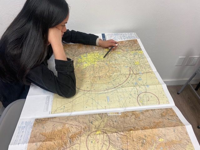 Person examining a large topographic map with a pencil while sitting at a table.