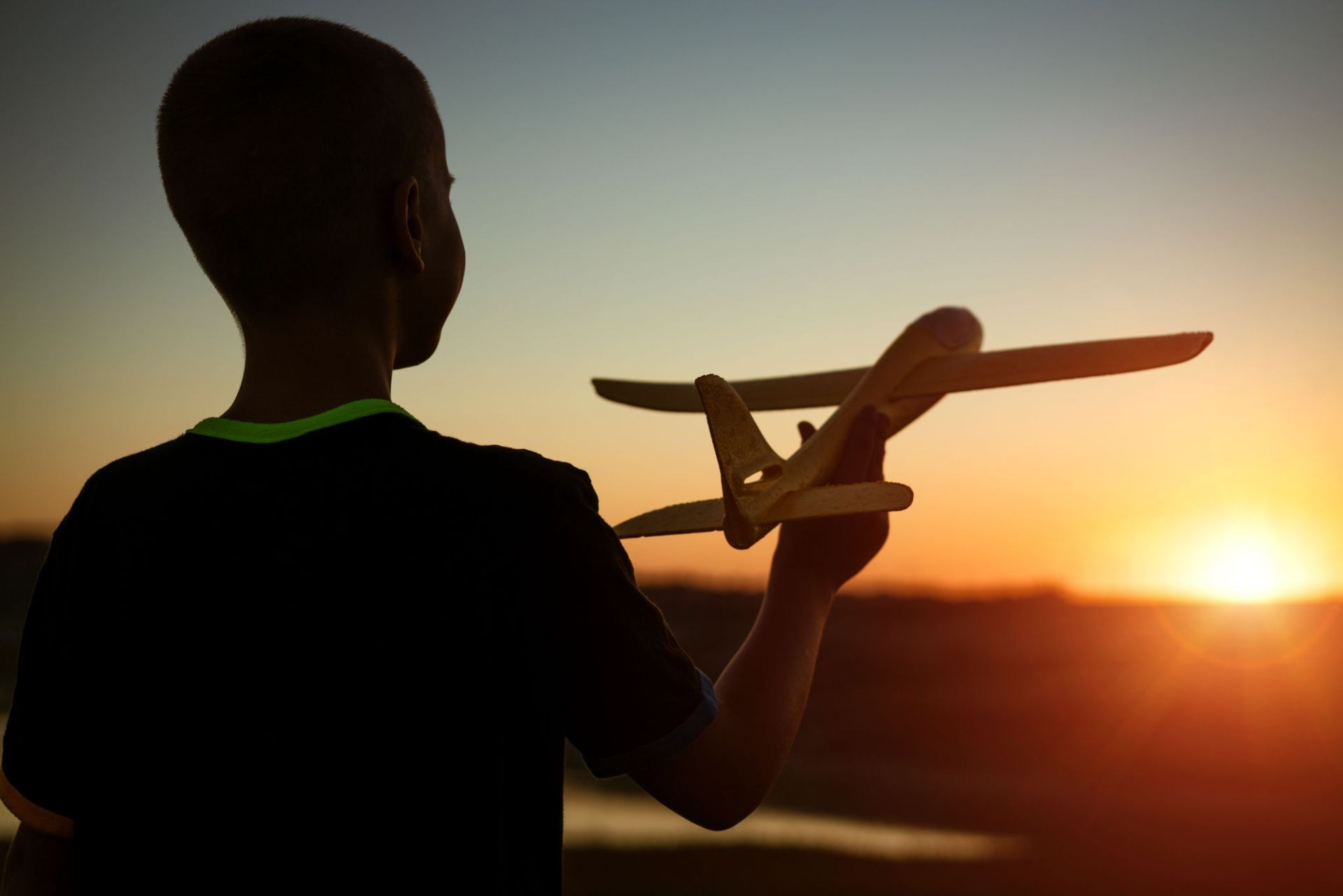 Silhouette of a child holding a toy plane against a sunset sky.