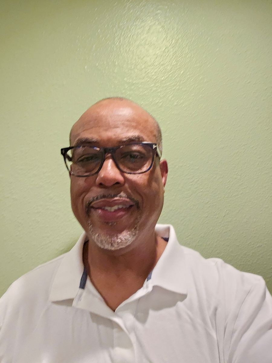 Person wearing a white polo shirt in front of a light green wall.